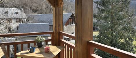 A wooden deck with a table and chairs, overlooking a mountainous landscape with buildings.