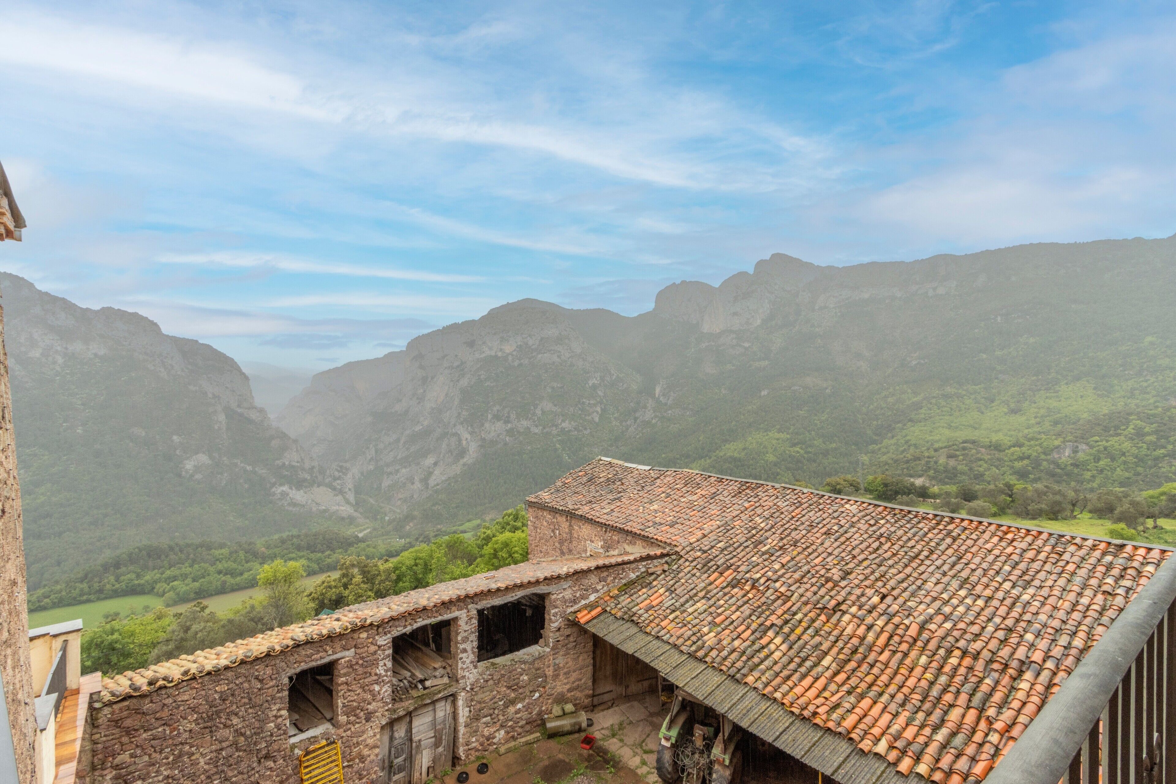 A rustic stone building with a tiled roof overlooking a valley.
