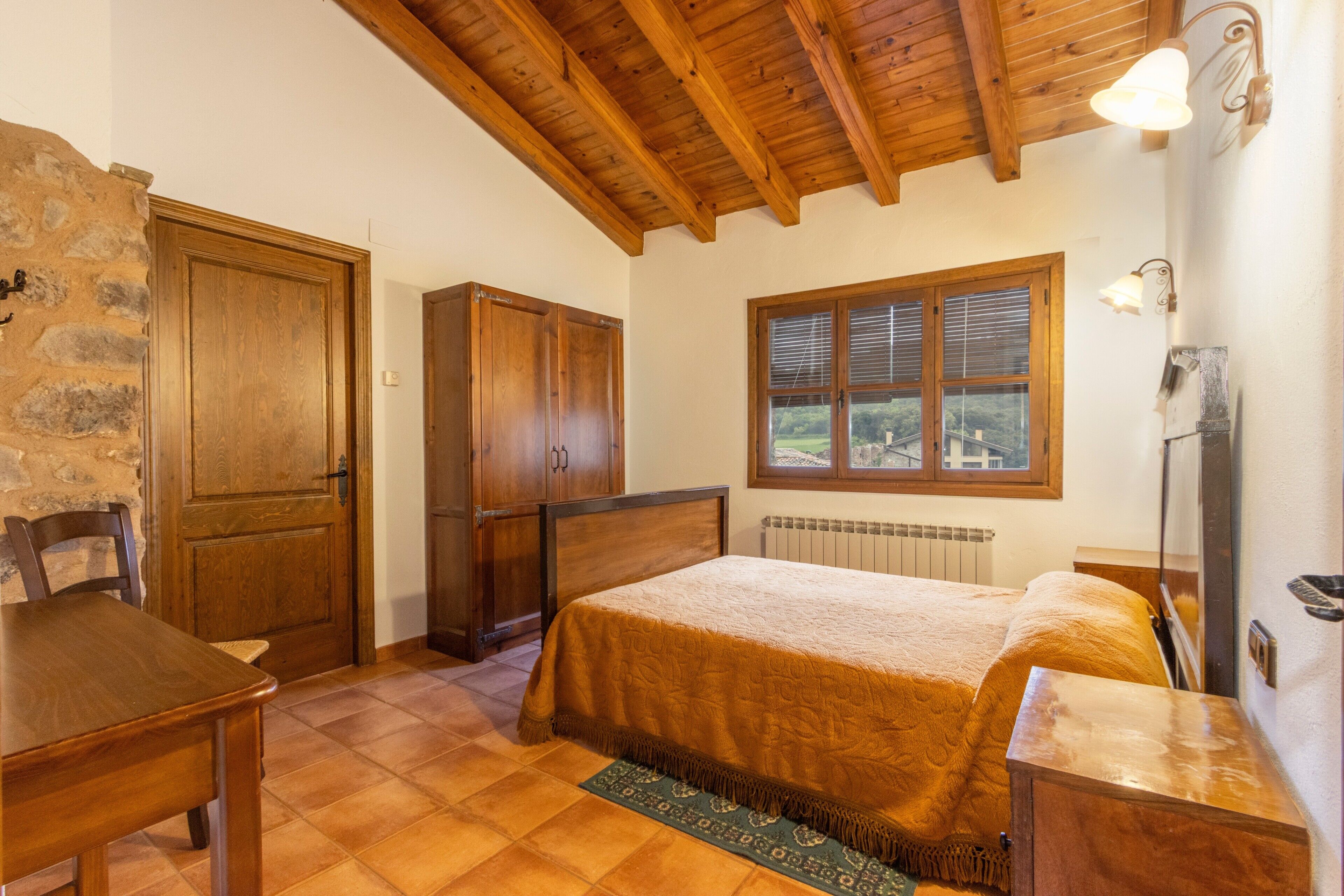 Una camera da letto con un letto di legno, un muro in pietra, una finestra con persiane e un termosifone.
