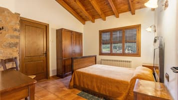 Una camera da letto con un letto di legno, un muro in pietra, una finestra con persiane e un termosifone.