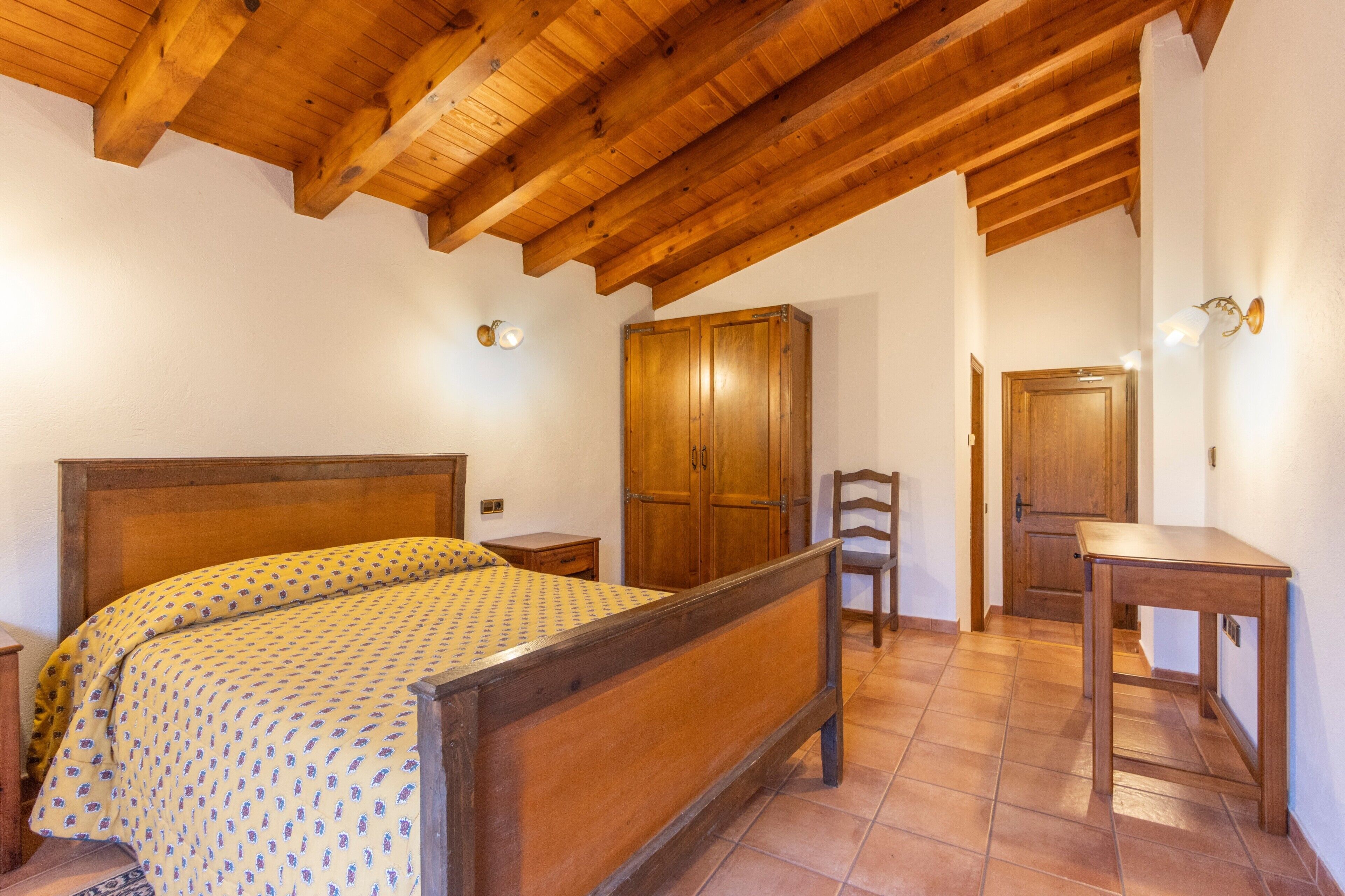 A bedroom with a wooden bed, a wardrobe, a chair, and a small table.