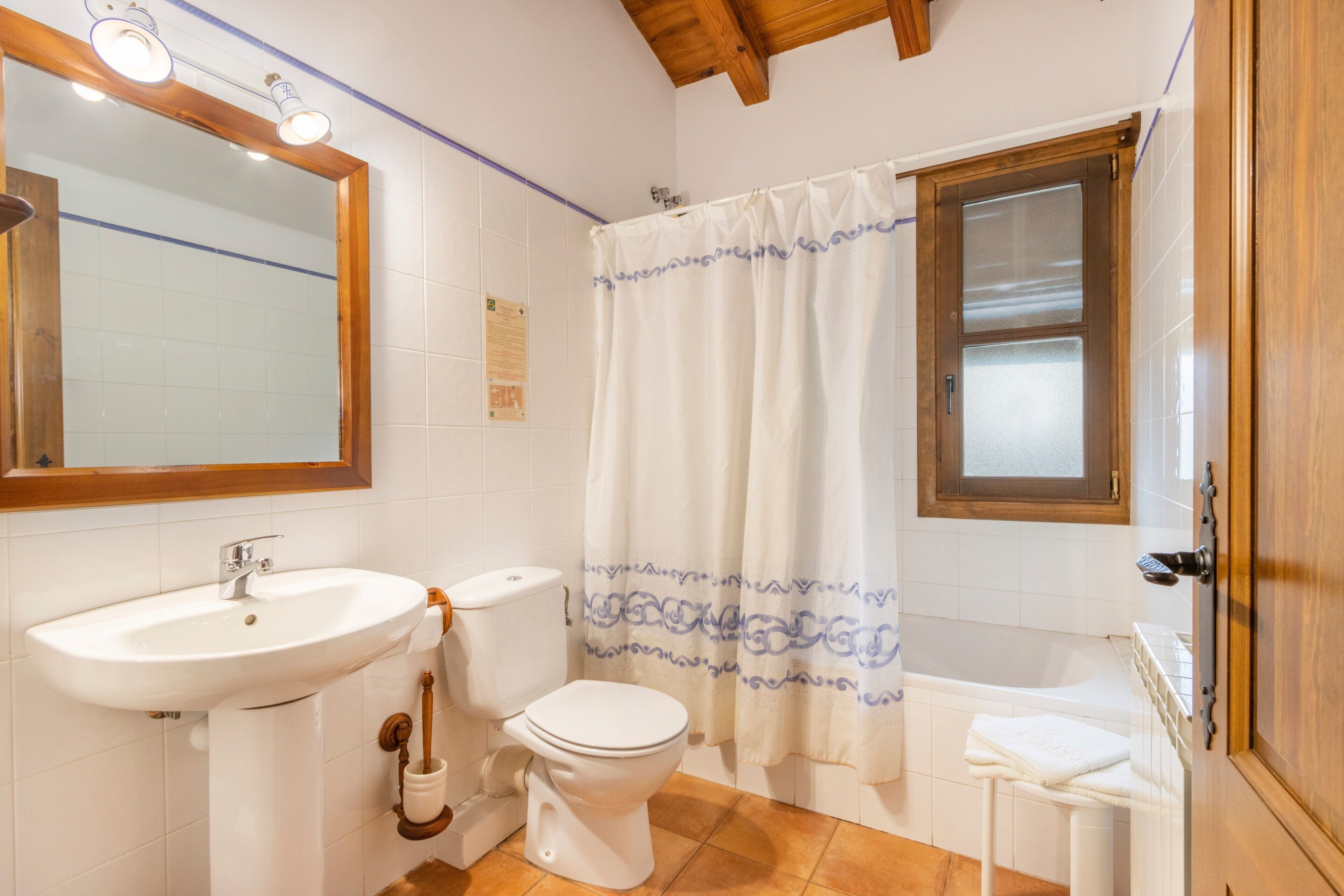 A bathroom with a sink, toilet, shower curtain, and a window.