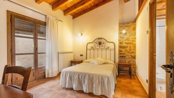 Un dormitorio con cama, una silla, una mesa, pared de piedra y techo de madera.