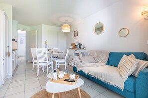 A living room with a blue sofa, white chairs, a coffee table, and a dining area with a table and chairs.