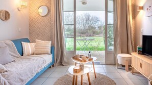 Una sala de estar con sofá, mesa de centro, televisor y vista a un jardín a través de un ventanal.
