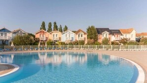 Una piscina de borde curvo, rodeada por una cerca blanca, y contigua a una hilera de casas coloridas.