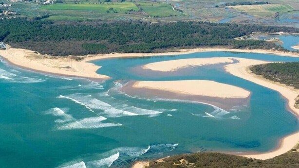 Vista aérea de una zona costera con playas de arena, aguas azules cristalinas y vegetación circundante.