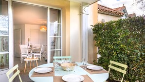Un área de comedor al aire libre con una mesa dispuesta para cuatro personas, rodeada de sillas y un arbusto grande al fondo.