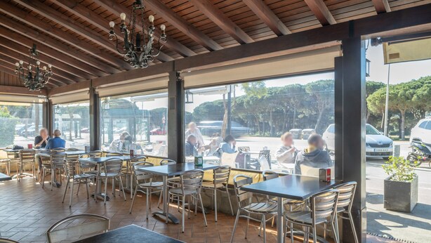 Een terras met tafels en stoelen, grote ramen en een houten plafond.