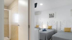 Hotelkamer met douche, twee bedden met hoofdeinden, een wandairconditioner en een ingelijste foto.
