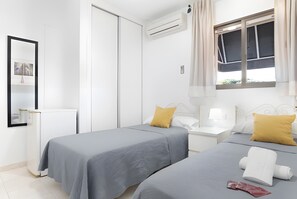Een hotelkamer met twee bedden, een nachtkastje met een lamp, een raam met gordijnen en een wandairconditioner.