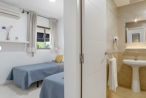 Een kamer met twee bedden, een raam met gordijnen, een wandairconditioner en een badkamer met wastafel en spiegel.