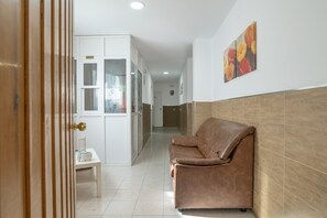 Un couloir avec un canapé en cuir marron, une armoire blanche et une petite table sur laquelle est posé un panneau.