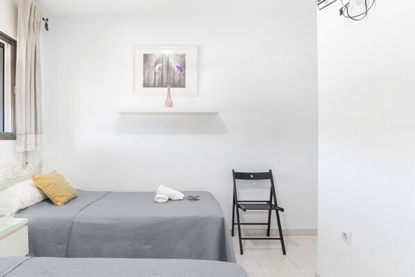 Une chambre d’hôtel avec deux lits, une chaise, une étagère avec un tableau et une fenêtre avec des rideaux.