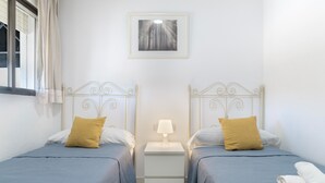 Een tweepersoonskamer met twee bedden, een nachtkastje, een lamp, een lijst met een afbeelding en een raam met gordijnen.