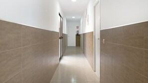 Un couloir aux murs et au sol carrelés, avec des portes de part et d’autre, et un extincteur fixé au mur.