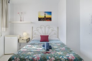 Une chambre à coucher avec un lit, une table de chevet, une lampe, une petite table avec un vase et un tableau représentant la Tour Eiffel.