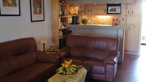 A living room with a brown leather sofa, a coffee table with fruit, and a kitchen in the background. - Apartment 'Gaby' with Sea Views, Wi-Fi and Air Conditioning (Denia)