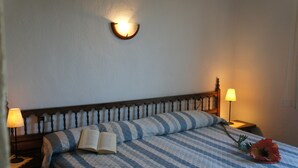 A neatly made bed with a striped quilt, a book, and a flower on it. There are two bedside lamps and a wall-mounted light fixture. - Apartment 'Gaby' with Sea Views, Wi-Fi and Air Conditioning (Denia)