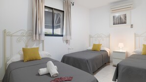 Hotelkamer met twee bedden, een raam met gordijnen, een airconditioner, een nachtkastje met een lamp en een inlijsting foto aan de muur.
