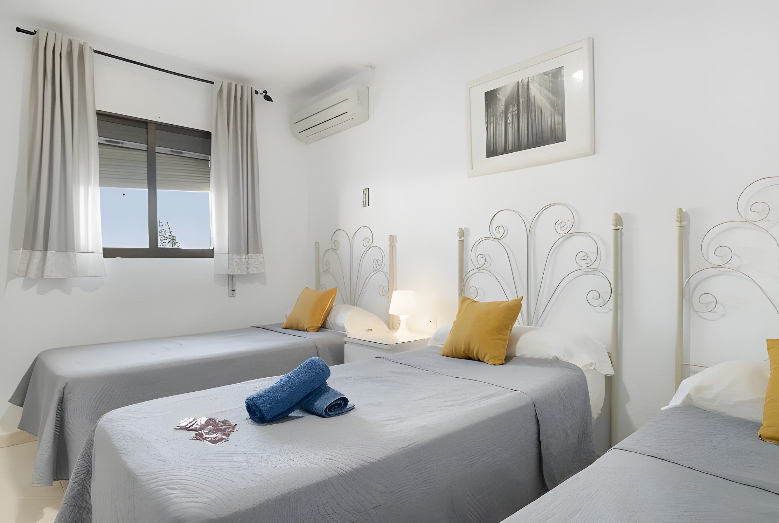 Habitación de hotel con dos camas individuales, una ventana con cortinas, un cuadro en la pared y un equipo de aire acondicionado.