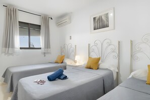 Een hotelkamer met twee enkele bedden, een raam met gordijnen, een lijst met een foto aan de muur en een airconditioning.