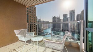 A balcony with white wicker furniture, a glass railing, and a view of a cityscape and water body. - Silkhaus Al Mass (Dubai)