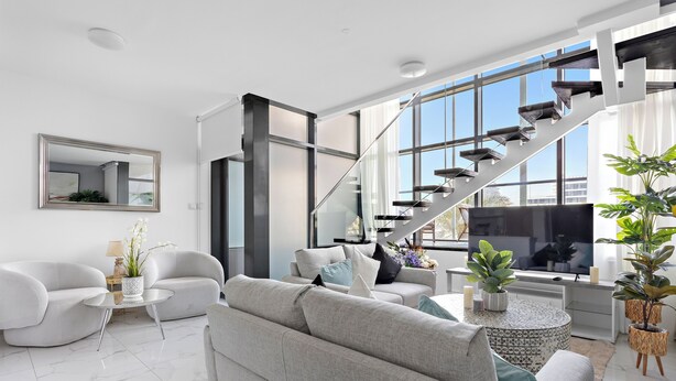 A modern living room with a staircase, white sofas, a TV, and potted plants. - Silkhaus Al Raha Lofts 2 (Abu Dhabi)