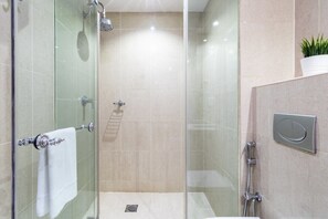 A modern bathroom with a glass-enclosed shower, a white towel on the door, and a small potted plant on the counter. - Silkhaus Al Tajer G (Dubai)