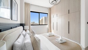 Habitación de hotel moderna con una cama grande, vistas a la ciudad, un armario y un cabecero.