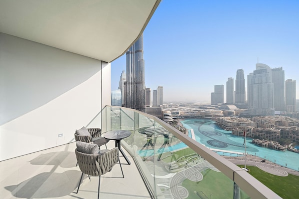A balcony with a glass railing overlooking a cityscape, including a prominent skyscraper.
