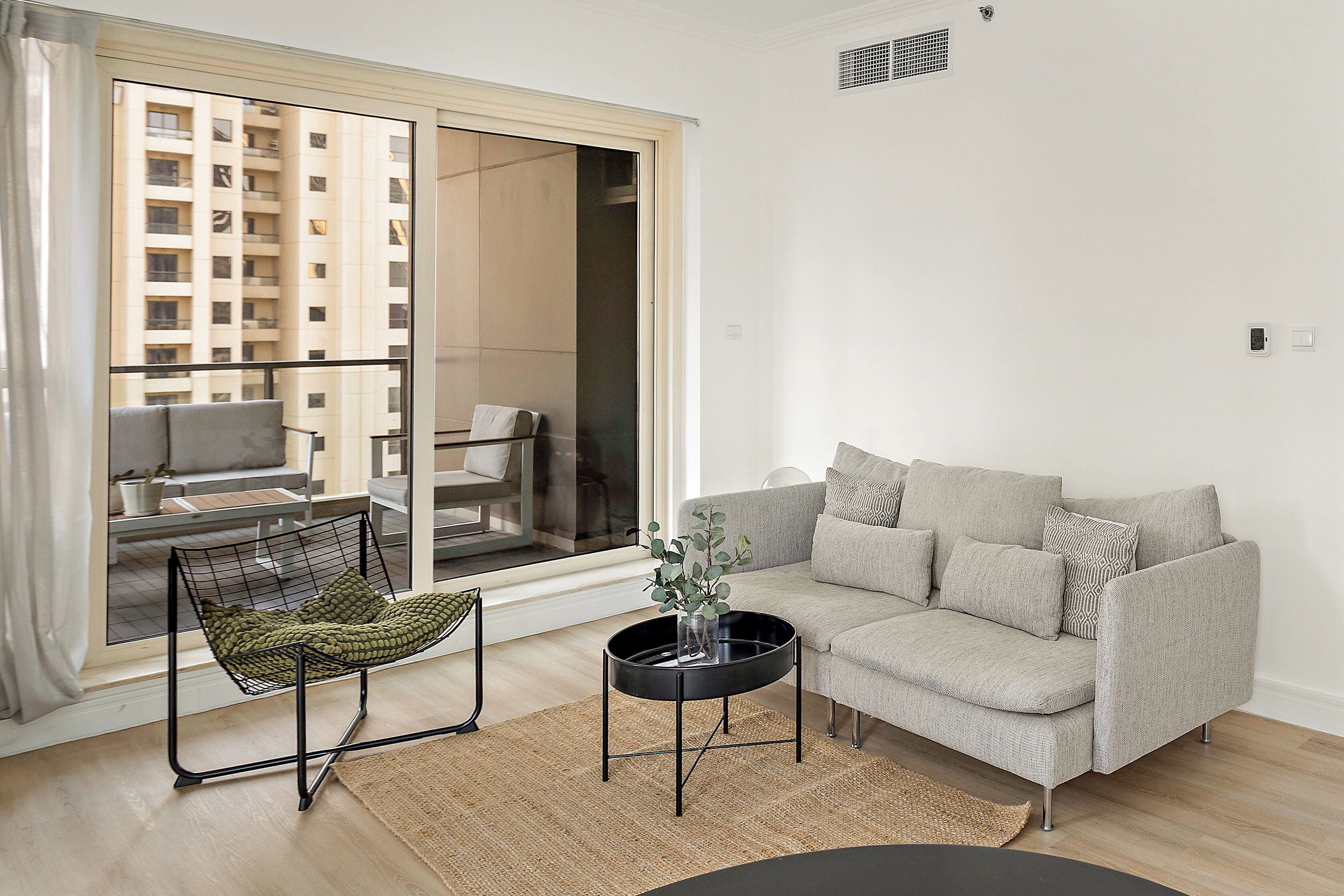 A modern living room with a grey sofa, a black coffee table, and a view of a balcony with a chair.