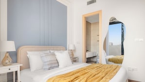 Habitación de hotel ordenada con cama, mesitas de noche, espejo y vista a la ciudad desde la ventana.