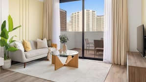 Una sala de estar moderna con un sofá, una mesa de centro de vidrio y vistas de edificios altos a través de amplios ventanales.