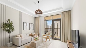 A modern living room with a sofa, coffee table, and armchair, a TV, and a large window with a view of buildings. - Silkhaus Reflection Tower (Abu Dhabi)