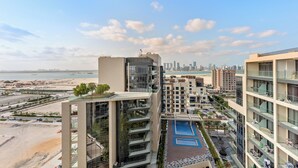 A high-rise building with multiple balconies overlooking a beach and a city skyline. - Silkhaus Soho Square (Abu Dhabi)