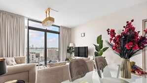 A modern living room with a sofa, a glass dining table, and a view of the city through large windows. - Silkhaus Soho Square (Abu Dhabi)
