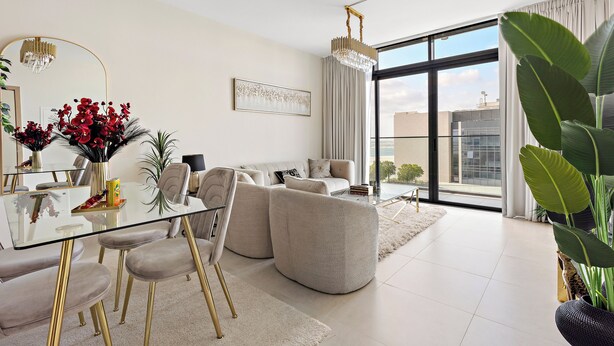 A modern living room with a glass dining table, beige sofas, and a large window offering a city view. - Silkhaus Soho Square (Abu Dhabi)