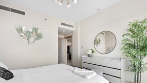 A modern bedroom with a neatly made bed, a dresser, a mirror, and a potted plant. - Silkhaus Soho Square (Abu Dhabi)