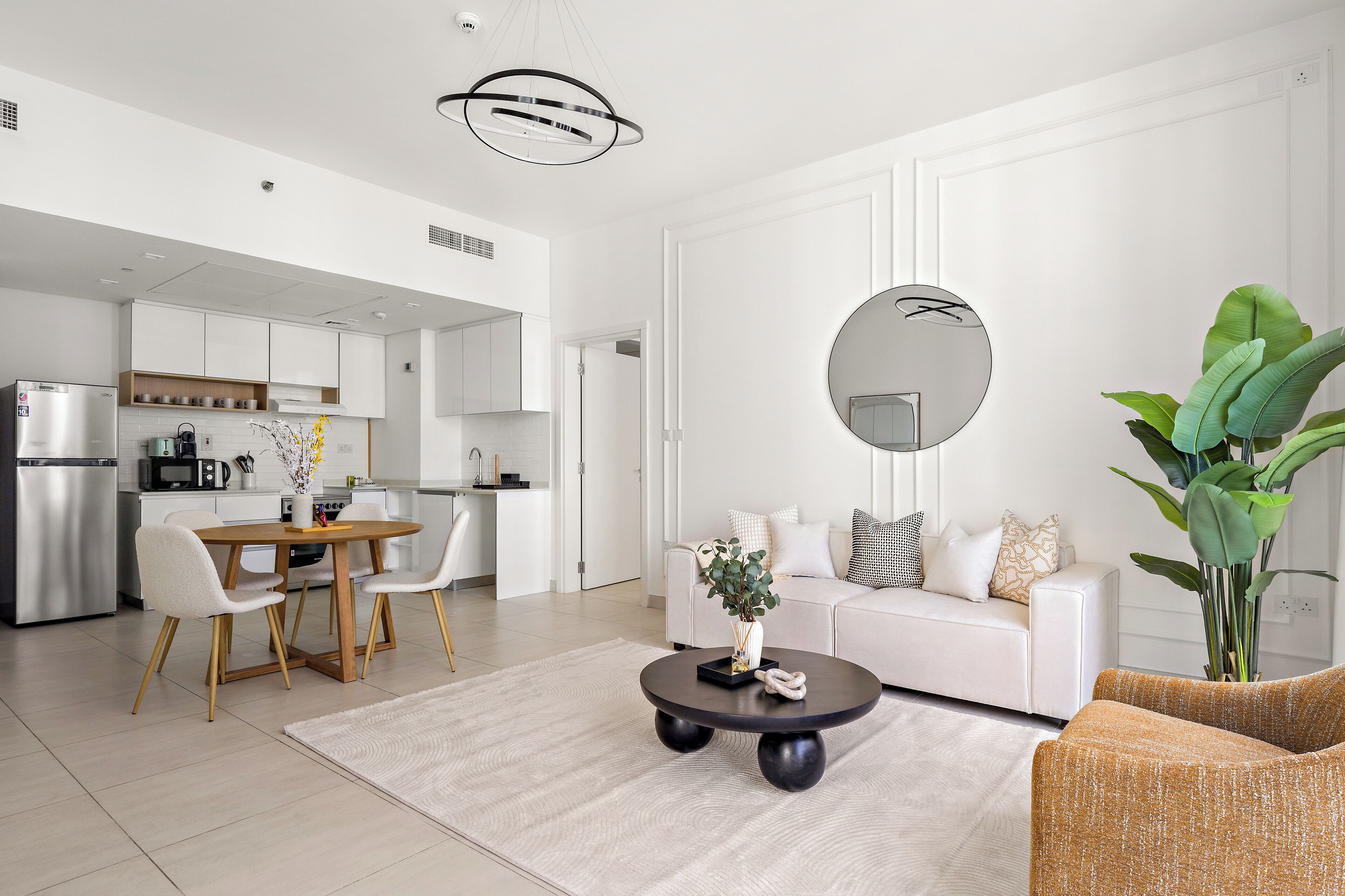Een moderne woonkamer met een witte bank, een ronde salontafel en een eethoek met een houten tafel en stoelen.