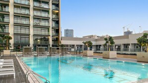 Ett modernt hotell med en pool på taket, flera balkonger och utsikt över stadens silhuett.