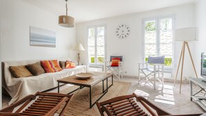 Un salón luminoso con un sofá, sillas de madera, una mesa de centro, una lámpara y un ventanal grande.