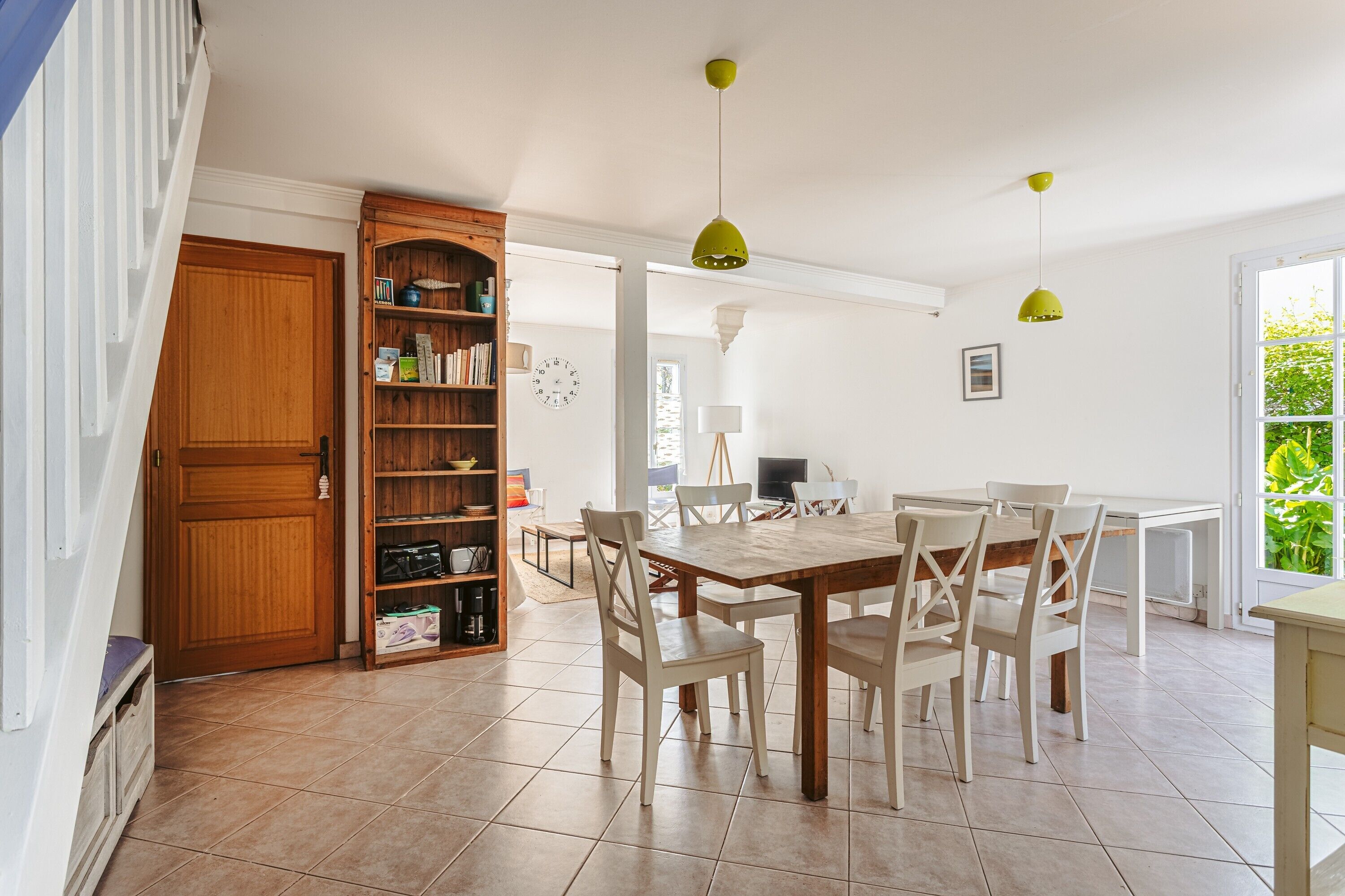 Un comedor con mesa y sillas de madera, una estantería y una ventana que da a zonas verdes.