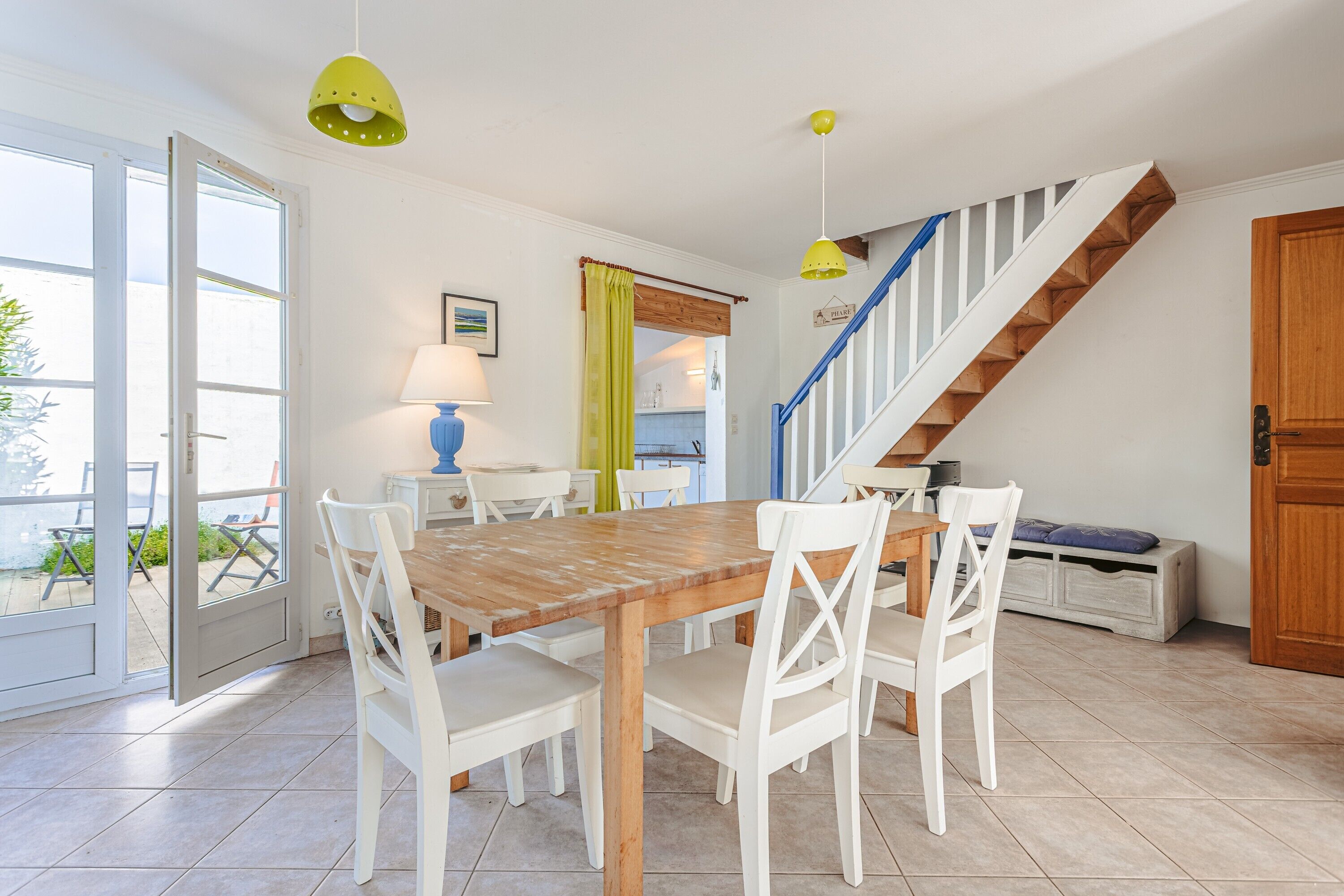 A dining area with a wooden table and white chairs, a staircase with wooden steps, and a door leading outside.