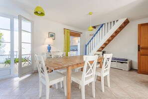 Een eetruimte met een houten tafel en witte stoelen, een trap met houten treden en een deur naar buiten.