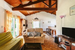 A living room with a sofa, a chair, a coffee table, a TV, and a wooden ceiling. - Charming Detached House with Terrace, Garden, and Garage 5 Minutes from the Beaches (Saint-Trojan-les-Bains)