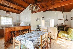 A cozy kitchen with wooden beams, a dining table with a newspaper tablecloth, and a yellow sofa. - Charming Detached House with Terrace, Garden, and Garage 5 Minutes from the Beaches (Saint-Trojan-les-Bains)