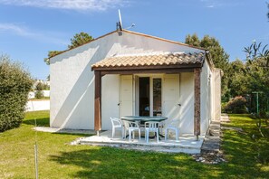 Um pequeno edifício térreo com telhado de telhas, um pátio com mesa e cadeiras e uma porta que dá para um espaço interno.