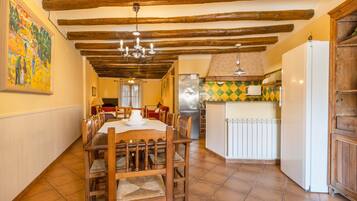 A dining area with wooden furniture, a chandelier, and a kitchen with a refrigerator and tiled backsplash.
