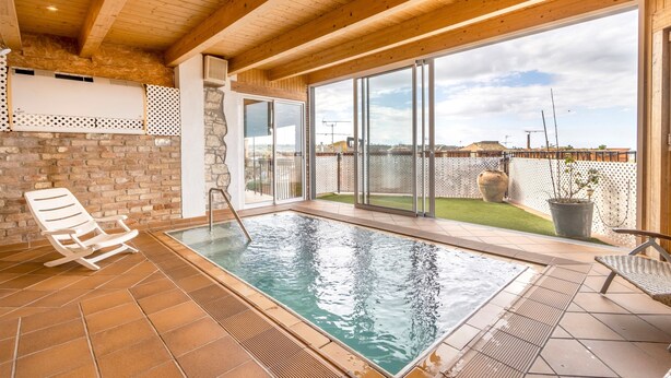 An indoor swimming pool with wooden beams, a brick wall, and a view of the city.